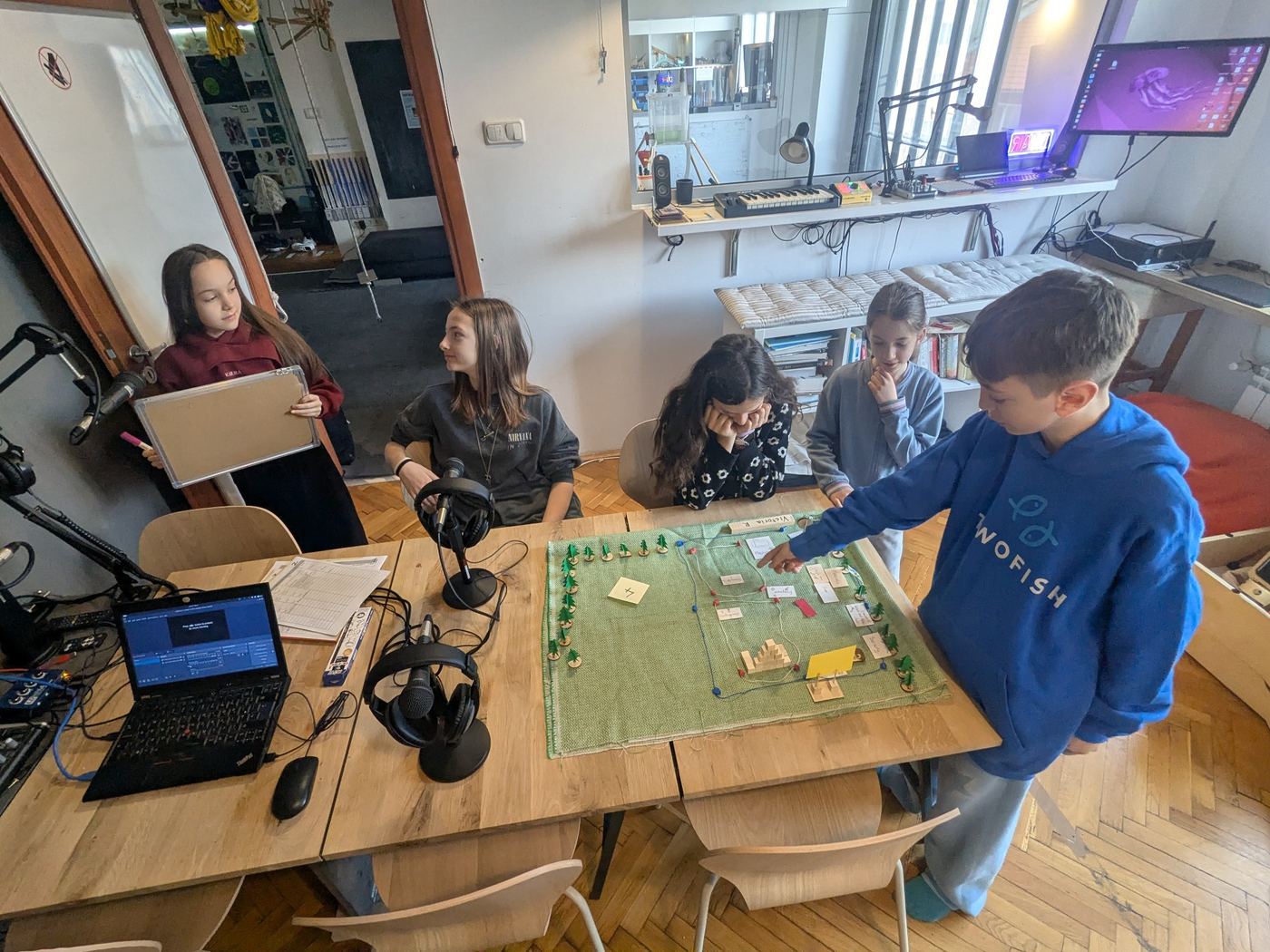 Children gathered around a table using a shared plan in a purposeful communication task.